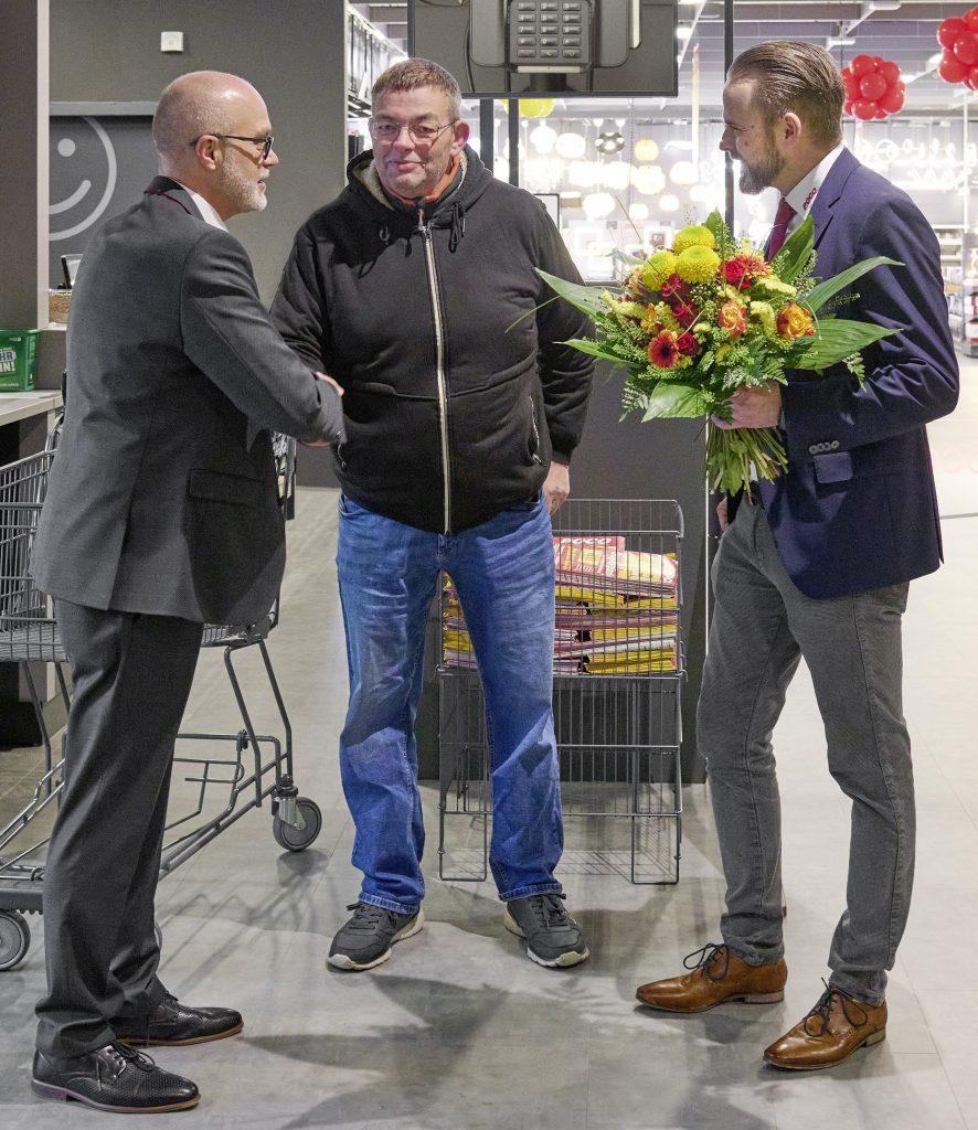 Mit einem Blumenstrauß begrüßte Marktleiter Daniel Schneider (re.) und Vertriebsleiter Stefano Buosi den ersten Kunden, Sven Ott, im neuer-öffneten POCO-Markt an der Rendsburger Straße. (Foto: POCO)
